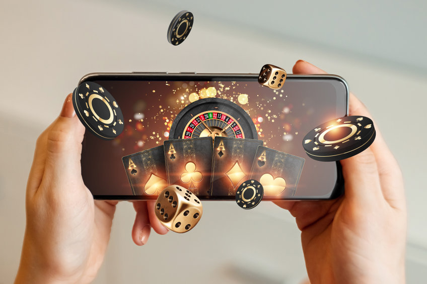 Creative background, online casino, in a man's hand a smartphone with playing cards, roulette and chips, black-gold background Internet gambling concept Copy space