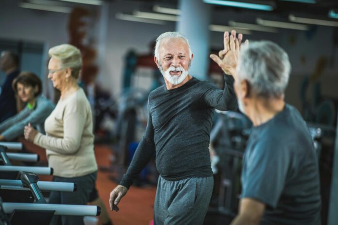 Happy senior men giving each other high five on treadmills in a gym