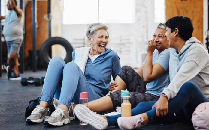 Gym, laughing and group of mature women telling joke after fitness class, conversation and comedy on floor Exercise, bonding and happy senior woman with friends sitting chatting together at workout